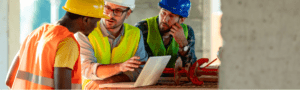 Three men on a building site looking at a laptop with construction insurance.