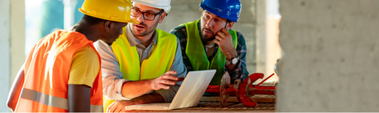 Three men on a building site looking at a laptop with construction insurance.